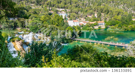 Aerial view of waterfall Skradinski Buk, Croatia. National nature park Krka. View of wooden bridge with tourists. Fresh green nature. Aerial view of waterfall Skradinski Buk, Croatia. National nature park Krka. View of wooden bridge with tourists. Fresh green nature. 136133891