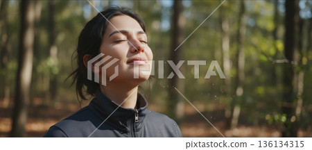 Woman Runner Pausing On Forest Trail, Catching Breath Under Sunlit Leaves After Steady Jog, Focused Posture And Relaxed Shoulders, Fitness And Nature Blend In Crisp Morning Air 136134315
