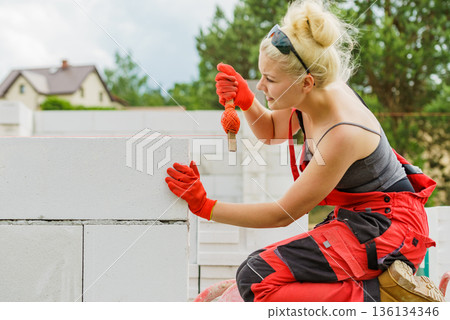 Woman using string as level in wall construction. Woman using string as level in wall construction. 136134346