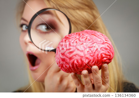 Woman holding magnifying glass investigating brain Woman holding magnifying glass investigating brain 136134360