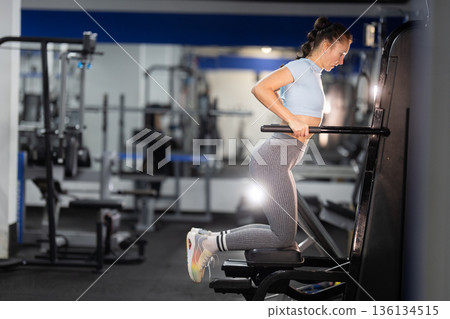 Woman exercising triceps on assisted dip machine 136134515