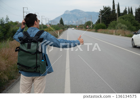 Tourist hitchhiking on a road with backpack and thumb up Tourist hitchhiking on a road with backpack and thumb up 136134575