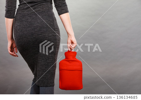 Woman holding warm red hot water bottle 136134685