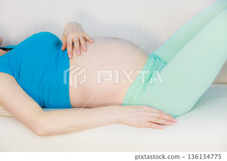 Pregnant woman lying on couch touching her belly Pregnant woman lying on couch touching her belly 136134775