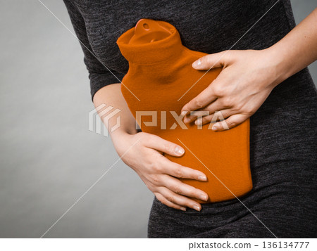 Girl having stomach ache, holding hot water bottle 136134777