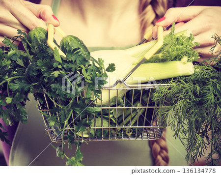 Woman in kitchen having vegetables holding shopping basket Woman in kitchen having vegetables holding shopping basket 136134778