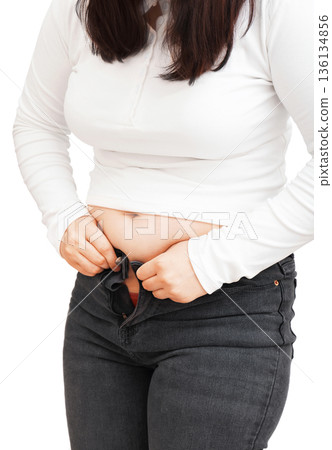 Overweight woman struggling to button tight jeans isolated on white background. Female trying to zip pants over belly. Diet and weight gain concept. High quality photo Overweight woman struggling to button tight jeans isolated on white background. Female trying to zip pants over belly. Diet and weight gain concept. High quality photo 136134856