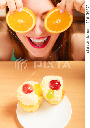 Woman with sweet cakes and orange covering eyes. Woman with sweet cakes and orange covering eyes. 136134875