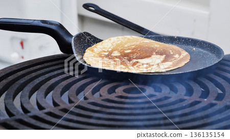 Pancake cooking on a hot skillet, releasing steam as breakfast food prepares 136135154