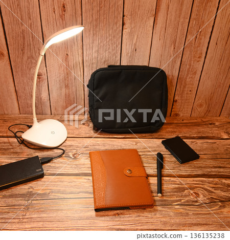 desk lamp shining on a notebook and a black bag desk lamp shining on a notebook and a black bag 136135238