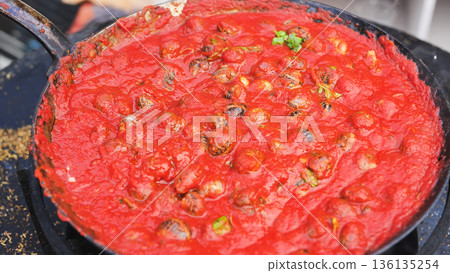 The chef pours oil over snails in tomato sauce. 136135254