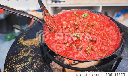 Snails cooking in tomato sauce over open fire 136135255