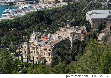 View of Malaga city hall Ayuntamiento de Malaga with clock tower, historic architecture and palm trees in park, cruise ship at harbor, Spain 136135337