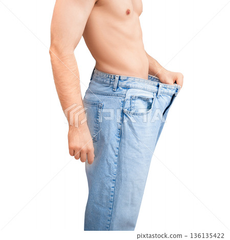 Slim man in oversized jeans showing successful weight loss results. Fit male pulling loose pants away from stomach isolated on white background Slim man in oversized jeans showing successful weight loss results. Fit male pulling loose pants away from stomach isolated on white background 136135422
