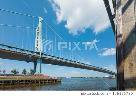 Benjamin Franklin bridge spans a body of water, with a blue sky above Benjamin Franklin bridge spans a body of water, with a blue sky above 136135780
