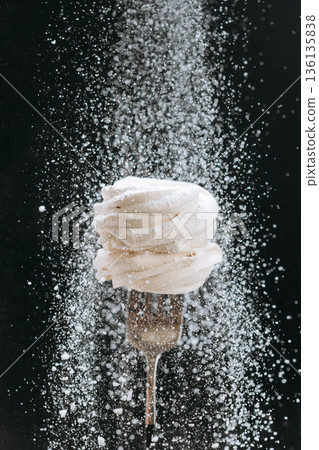 White zephyr on fork with falling powdered sugar on dark background 136135838