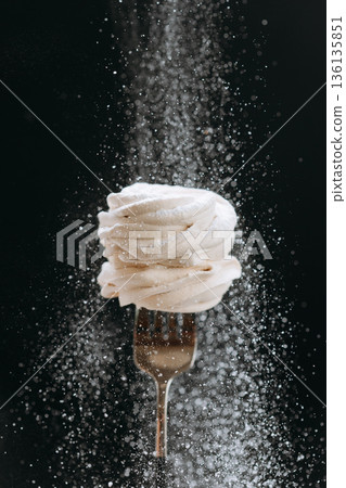 White zephyr on fork with falling powdered sugar on dark background White zephyr on fork with falling powdered sugar on dark background 136135851