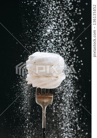 White zephyr on fork with falling powdered sugar on dark background White zephyr on fork with falling powdered sugar on dark background 136135852