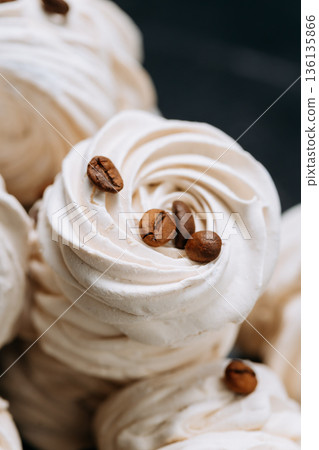 Macro of white meringue swirls topped with coffee beans on dark background 136135866