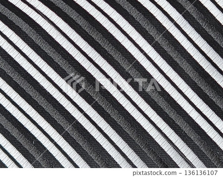 Close-up of fabric of a men's tie with diagonal black and silver stripes. The accessory is made of microfiber Close-up of fabric of a men's tie with diagonal black and silver stripes. The accessory is made of microfiber 136136107