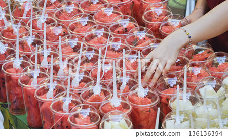 Woman's hand picking watermelon fruit salad cups in a vibrant street market Woman's hand picking watermelon fruit salad cups in a vibrant street market 136136394