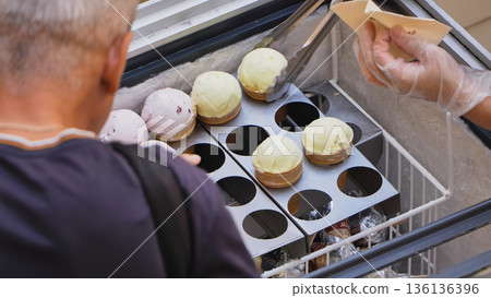 Customer choosing flavored ice cream cones from a street food vendor freezer Customer choosing flavored ice cream cones from a street food vendor freezer 136136396