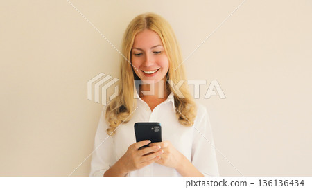happy young woman with mobile phone looking at device 136136434