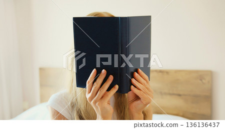 Young sad tired woman student with open book lying on the bed at home 136136437
