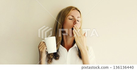 Sleepy lazy woman yawns waking up after sleeping holds cup of coffee in morning on white background 136136440