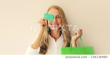 Portrait of happy smiling middle aged woman holding plastic credit bank card with shopping bags Portrait of happy smiling middle aged woman holding plastic credit bank card with shopping bags 136136460