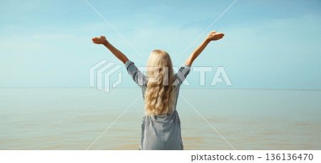 Summer vacation, happy inspired young woman raising her hands up on the beach, relaxed girl on sea Summer vacation, happy inspired young woman raising her hands up on the beach, relaxed girl on sea 136136470