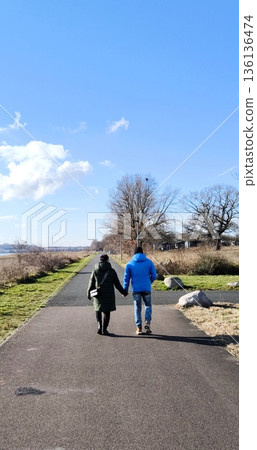 A loving couple walks hand in hand along an asphalt path in a park on a sunny day 136136474