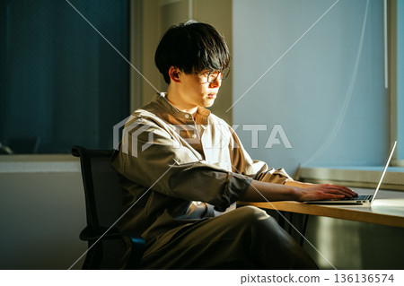 日落時分,一位年輕男子在窗邊工作。 日落時分,一位年輕男子在窗邊工作。 136136574