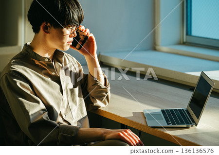 A young man talking on his smartphone while looking at a computer A young man talking on his smartphone while looking at a computer 136136576