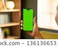 Person holding a mobile phone with a chroma key green screen, suitable for displaying various apps, videos, or messages, highlighting concepts of technology, connectivity, and communication 136136653