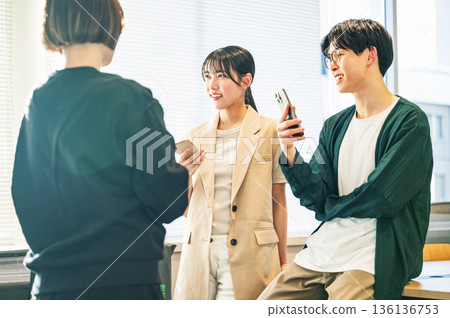 年輕男女一邊聊天一邊拿著智慧型手機 136136753