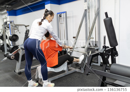 Personal trainer guiding woman during gym workout 136136755