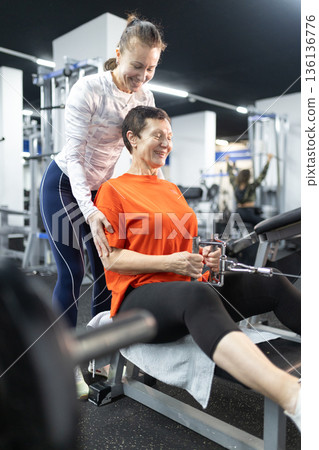 Personal trainer guiding senior woman during gym workout Personal trainer guiding senior woman during gym workout 136136776