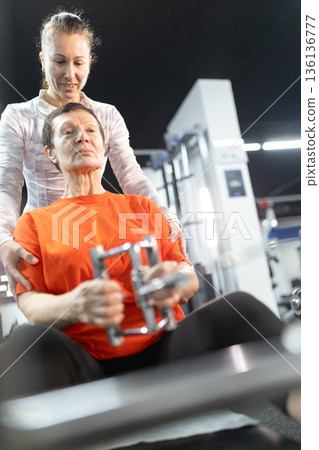 Senior woman exercising with personal trainer support 136136777