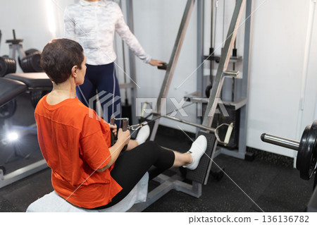 Mature woman training back muscles with gym machine 136136782