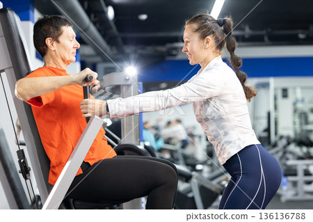 Senior woman training chest press with personal trainer guidance 136136788