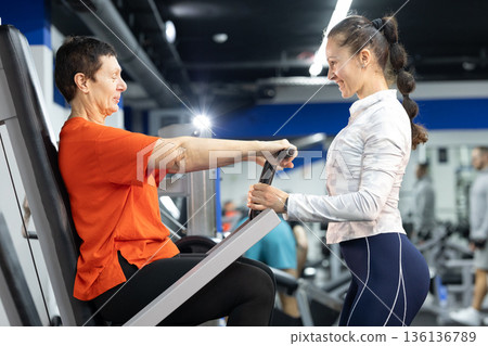 Senior woman exercising chest press with personal trainer 136136789