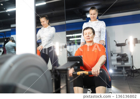 Senior woman exercising on rowing machine with instructor Senior woman exercising on rowing machine with instructor 136136802