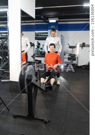 Senior woman exercising on rowing machine with personal trainer Senior woman exercising on rowing machine with personal trainer 136136804