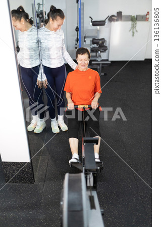 Personal trainer guiding senior woman on rowing machine Personal trainer guiding senior woman on rowing machine 136136805