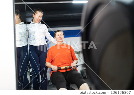 Senior woman exercising on a rowing machine with a personal trainer Senior woman exercising on a rowing machine with a personal trainer 136136807