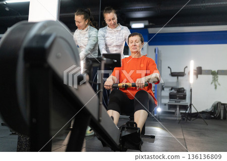 Senior woman exercising on a rowing machine with coach Senior woman exercising on a rowing machine with coach 136136809