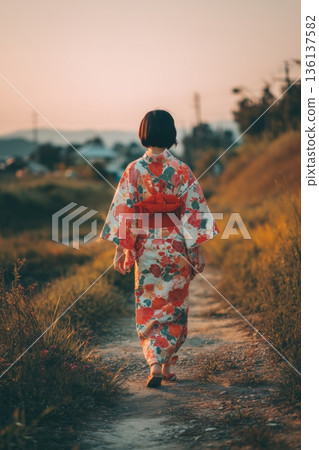 一位身穿花卉圖案浴衣的女子在黃昏時分漫步於小徑上，展現出夏日日式風情。 136137582