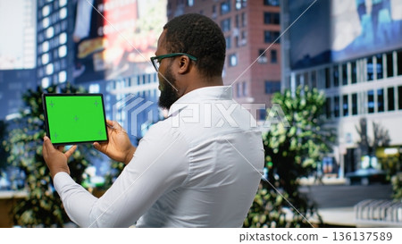 Horizontal green screen held by adult male walking on the sidewalk, enjoying a stroll in the city center surrounded by skyscrapers and office buildings. Urban streets. Camera B. Horizontal green screen held by adult male walking on the sidewalk, enjoying a stroll in the city center surrounded by skyscrapers and office buildings. Urban streets. Camera B. 136137589