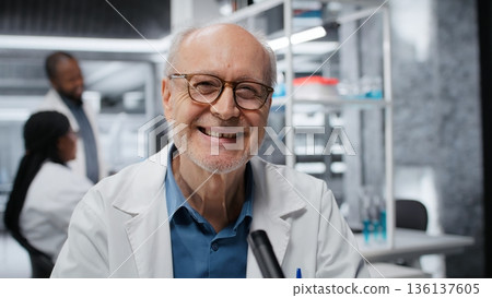 Smiling senior biologist in medical laboratory using scientific microscope for cellular analysis. Jolly elderly man examining sample in lab with high tech optical device gear, camera B Smiling senior biologist in medical laboratory using scientific microscope for cellular analysis. Jolly elderly man examining sample in lab with high tech optical device gear, camera B 136137605